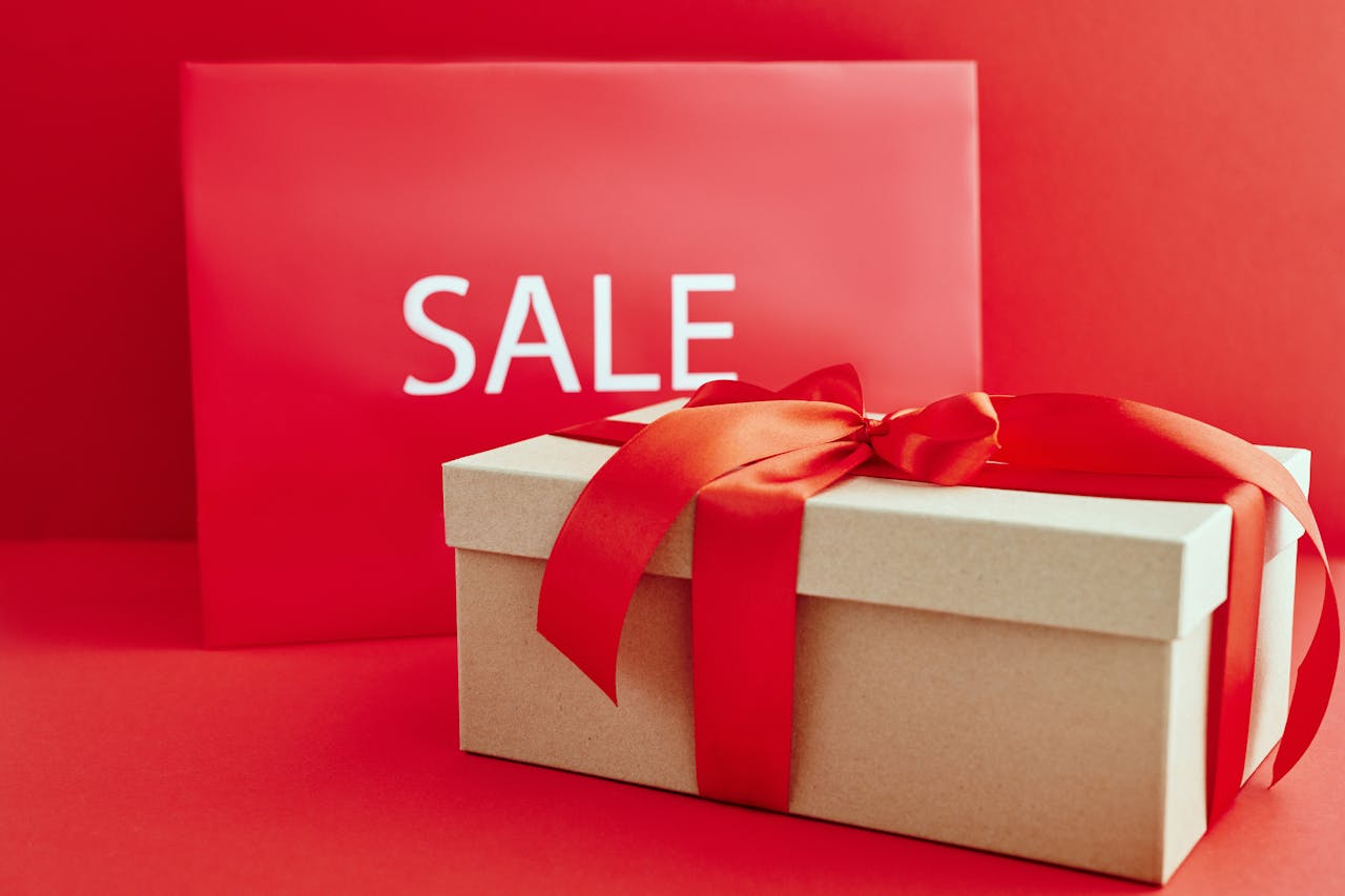 creative-02 Gift box with red ribbon on red background with sale sign, perfect for retail promotions.